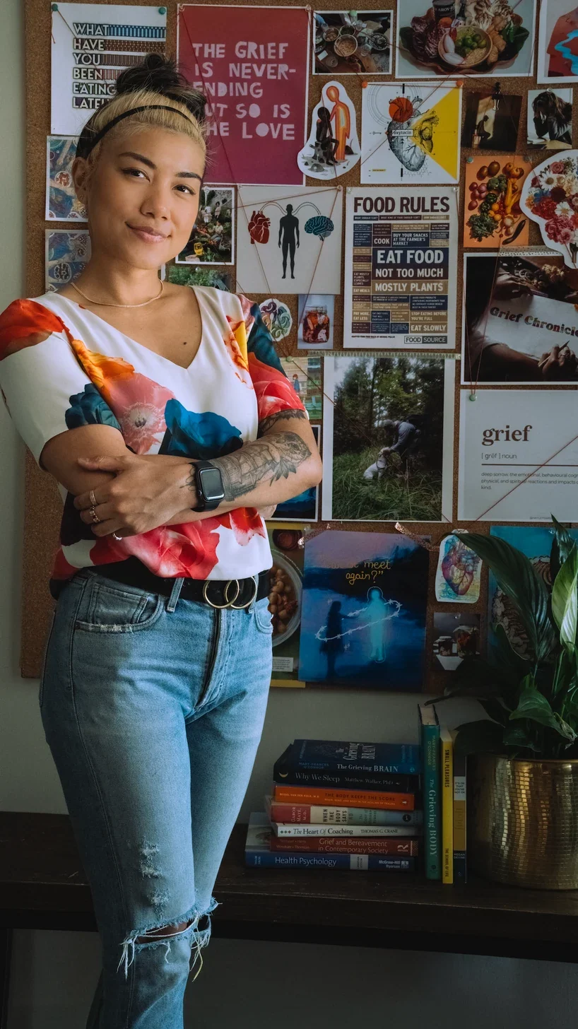 Vera Decena standing in front of her grief mood-board wall, arms crossed, smiling